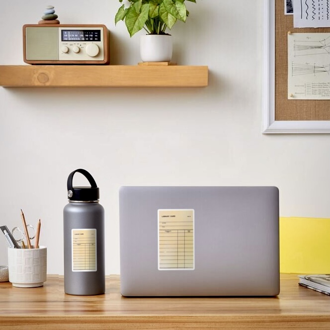 Laptop and water bottle with stickers featuring vintage library card artwork 